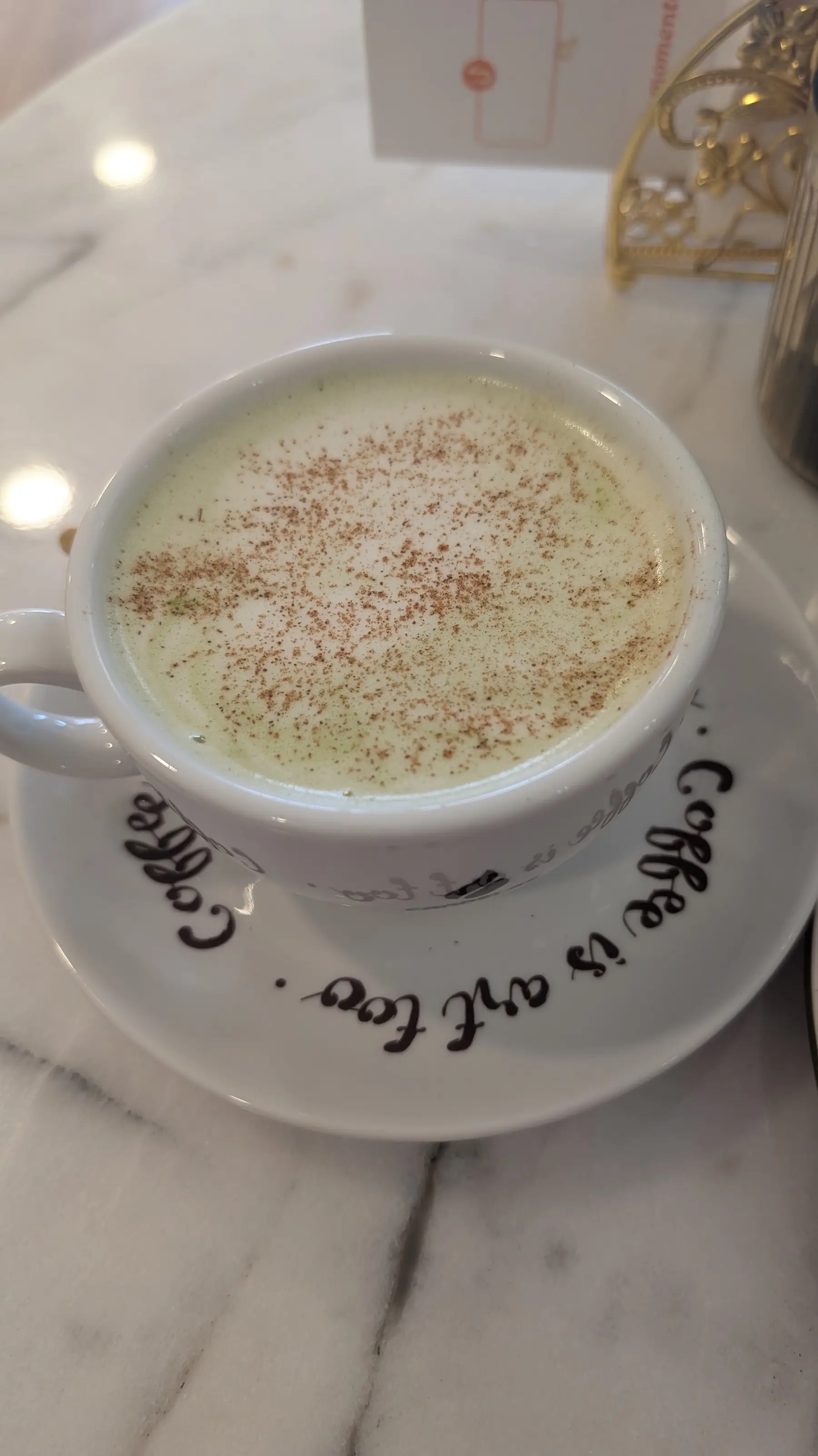 Capuchino con canela en una taza blanca; el platillo dice «Coffee is art too.»